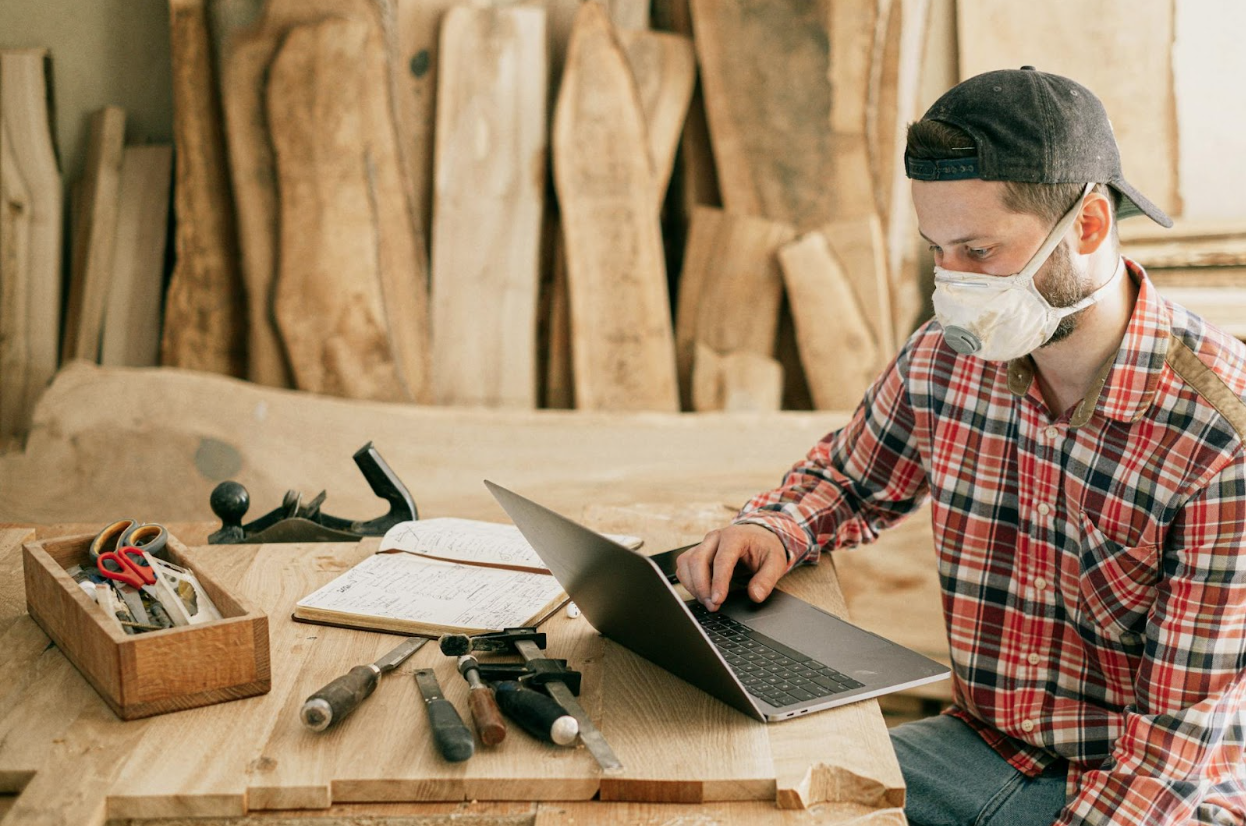 A man using a laptop at a wood workshop, working on his debt strategy.