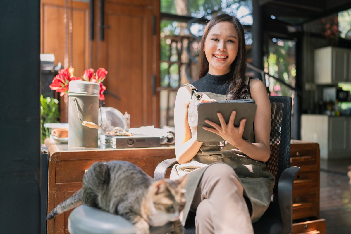 A woman sitting with a tablet and reviewing bills in her shop.