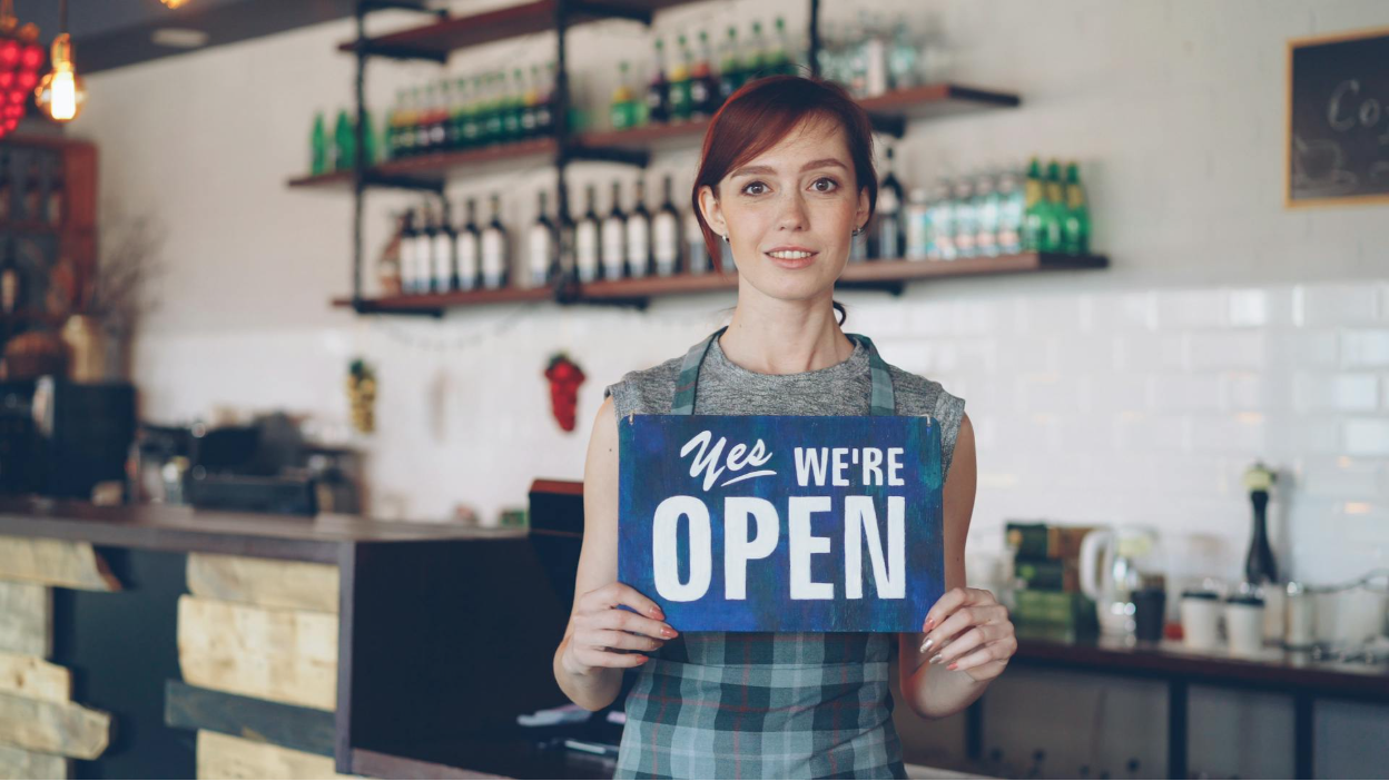 A business owner holding a “Yes we’re open” sign.