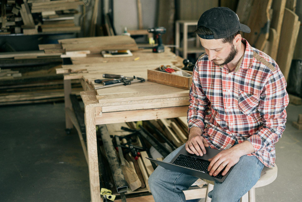 A carpenter sitting in his shop and working on his business strategy on a laptop.